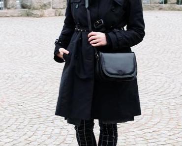 Übergangsoutfit mit schwarzem Trenchcoat, Musterhose und Stiefeletten
